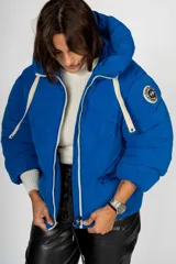 Campera puffer azul con capucha, cierre frontal con cremallera y bolsillos laterales.