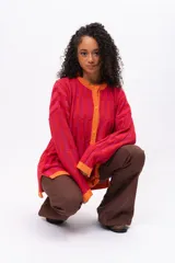 Saco de punto con diseño de bloques de color en tonos rojos y fucsias, con terminaciones en color naranja. Presenta cuello redondo, cierre frontal con botones y mangas largas.