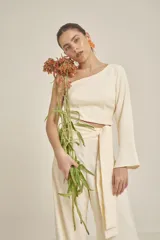 Top color crema con un solo hombro, manga larga acampanada y corte crop.