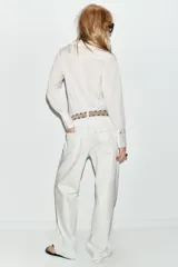 Camisa de manga larga con estampado de rayas verticales finas, cuello redondo con volante plisado y detalle de volante lateral en el frente. Cuenta con cierre frontal de botones y puños anchos.