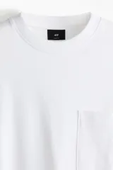 Remera de manga larga en punto pesado de algodón, color blanco, con cuello redondo ribeteado acanalado, hombros caídos, bolsillo superior abierto y bajo recto. Corte holgado.