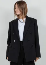 Blazer oversize negro con un sutil brillo, solapas de muesca, doble botonadura frontal y bolsillos con solapa.