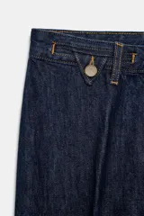 Jeans de tiro alto con corte flare y ajuste slim. Presenta trabillas en la cintura, bolsillos delanteros con detalle de botones metálicos y raya planchada a lo largo de las piernas. Cierre frontal con cremallera y botón.
