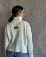 Sweater de lana color crudo con cuello alto y diseño trenzado.