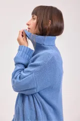 Sweater de punto color azul, con cuello alto y diseño de trenzas verticales. Presenta mangas largas con puños acanalados y un corte holgado.