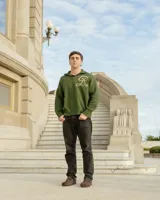 Sweater tejido de algodón en color verde oscuro, con cuello alto y cierre frontal parcial. Presenta un diseño de letra R bordada en color beige en el frente.