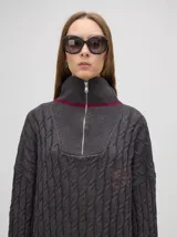 Pullover gris de algodón con tejido en ochos, cuello alto con cierre frontal parcial y puños a rayas.