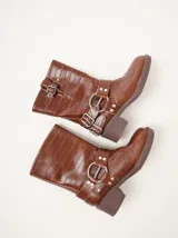 Botas de caña media Mutma modelo Mota, confeccionadas en cuero texturado color marrón. Presentan diseño de punta cuadrada, taco de 5 cm, múltiples tiras con hebillas metálicas ajustables y herrajes circulares en los laterales.