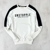 Buzo blanco de algodón con mangas raglán negras y estampa frontal con la palabra "UNSTOPPLE" y la frase "DUXON COLLECTION" en negro.