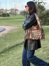 Cartera tipo shopper confeccionada en cuero marrón y detalles en pelo con estampado animal print tipo vaca, con bolsillos exteriores y tiras colgantes decorativas.