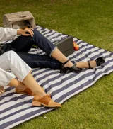 Zapato de cuero vacuno color gris topo, con talón descubierto y pulsera con hebilla. Tiene taco de madera forrado en cuero y suela de goma. La horma es de punta cuadrada, ancha y cómoda.