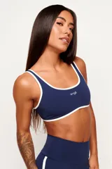 Top deportivo de poliamida color azul marino, de modelado slim y ajuste ceñido al cuerpo. Presenta escote redondo y tiras en color blanco contrastante que recorren los bordes superior e inferior, con el logo de la marca estampado en el centro del pecho.