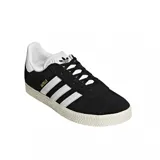 Championes urbanos Adidas modelo Gazelle, color negro con las icónicas tres tiras laterales y refuerzo en el talón en color blanco. Presenta el nombre del modelo en letras doradas en el lateral y suela de goma texturizada en color crema.