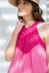 Vestido corto de color rosado con escote halter tejido en crochet de algodón. Presenta un diseño suelto con falda de volados escalonados.