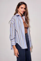 Camisa de corte oversize con estampado de rayas verticales en tonos azul claro y mostaza. Presenta cuello clásico, cierre frontal con botones y mangas largas con puños abotonados.