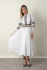 Vestido midi blanco con detalles de encaje y vivos negros. Tiene cuello mao, mangas largas con puños de encaje y falda amplia con tul de armar.