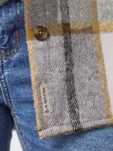 Sobrecamisa de corte holgado con estampado de cuadros en tonos gris, blanco y mostaza. Presenta cuello clásico, cierre frontal con botones, mangas largas con puños abotonados y bolsillos frontales con solapa.
