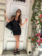 Vestido corto negro con escote halter y cierre frontal con cremallera dorada.