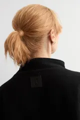 Capa de corte amplio y diseño bicolor, combinando negro en la parte frontal y trasera con paneles laterales en color beige. Presenta cuello alto y cierre frontal con hebilla metálica.
