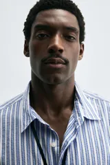 Camisa regular fit de lyocell con efecto arrugado, cuello solapa, manga larga con puño de botón, bolsillo plastrón en el pecho y cierre frontal de botonadura. Presenta un patrón de rayas verticales en tonos azules y blancos.