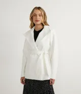 Campera alargada de polivelour color blanco, con cuello alto que se pliega y se ata a la cintura, mangas largas, abotonado frontal doble, bolsillos y cinturón.