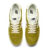 Championes New Balance modelo 500, color verde mostaza, con logo 'N' blanco en el lateral. Presentan una estructura de ante y nobuk con detalles perforados en la puntera y una entresuela de goma de color crema.