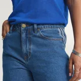 Pantalón Adidas Firebird de denim azul de corte holgado, con tiro medio y las icónicas tres tiras blancas a lo largo de los laterales de las piernas.