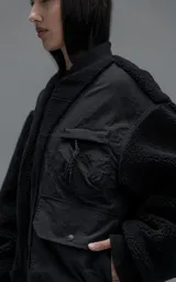 Campera estilo bomber unisex, confeccionada en una combinación de corderito sintético y paneles de ripstop. Presenta un diseño utilitario con múltiples bolsillos frontales con cierres y broches a presión, cuello, puños y ruedo en ribb elástico.