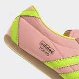 Championes Adidas modelo Tokyo de estilo retro, con exterior de nylon en color rosado y detalles en amarillo neón en las tres tiras laterales y el talón. Presenta una suela de caucho en tono marrón y un diseño de corte bajo.