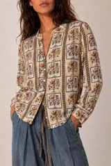 Camisa de manga larga color beige con estampado geométrico y floral en tonos marrones y naranjas, escote en V y botonadura frontal.