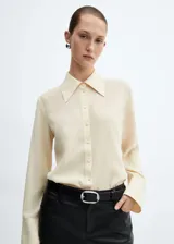 Camisa color crema de corte recto, cuello camisero y mangas largas con puños abotonados.