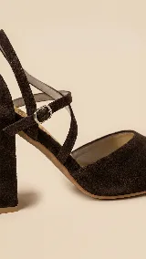 Zapato de tacón alto en gamuza color verde oliva, con diseño de punta fina y escote en V. Presenta tiras cruzadas en diagonal con cierre de hebilla ajustable en el tobillo y taco cuadrado.