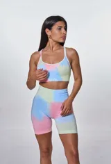Conjunto deportivo compuesto por un top de escote redondo con breteles finos y un short ciclista de tiro alto. Ambas piezas presentan un diseño estampado estilo tie-dye en tonos pastel de azul, rosa y verde, con el logo de la marca estampado en el frente del top.