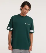 Remera verde oscura de corte relaxed, con cuello redondo y mangas cortas adornadas con dos líneas blancas paralelas. Presenta un pequeño estampado tipográfico blanco en el pecho con las siglas N.Y.U.S.