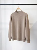 Buzo de punto en color beige, con cuello redondo alto y mangas largas con diseño raglán. Presenta puños y cuello acanalados.
