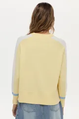 Sweater de punto color blanco con mangas raglán en azul y detalles en verde en los puños, cuello redondo y bordado de libélula en el pecho.