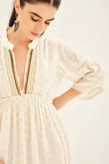 Vestido corto blanco con estampado de puntos dorados, mangas al codo con volados y ajuste en la cintura. Escote en V con detalles bordados en dorado y negro.