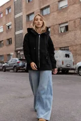 Campera tipo gabardina color negro, con capucha, cierre frontal metálico y bolsillos delanteros amplios. Presenta un diseño urbano con cintura ajustable y calce relajado.