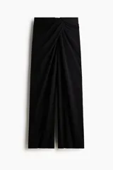 Pantalón de tiro alto negro, de corte holgado y pernera recta, confeccionado en punto grueso. Presenta un diseño drapeado con un detalle de nudo o giro en la parte frontal de la cintura.