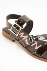 Sandalias de cuero charolado negro con dos tiras con hebillas metálicas plateadas y tira en el talón. Suela plana color marrón.