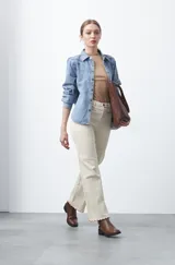 Pantalón de fit recto color beige claro, confeccionado en cotton spandex. Presenta costuras visibles que recorren la pierna y bordados decorativos en la zona de la cintura. El ruedo del pantalón tiene un borde festoneado.