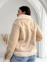 Chaqueta color beige con interior de piel sintética blanca, cierre cruzado con cremallera y detalles de hebillas en los puños.