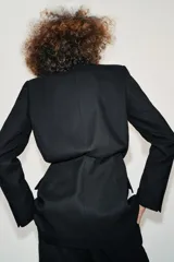 Blazer de cuello solapa y manga larga con hombreras marcadas. Presenta un diseño cruzado con cierre frontal de botones a presión, bolsillos delanteros con solapa y un detalle de cintura entallada con efecto abullonado.
