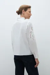 Camisa blanca de manga larga con cuello alto fruncido y bordados calados en el pecho y los hombros.