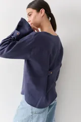 Blusa de lino con cuello bote y mangas largas terminadas en puños acampanados con volados. Presenta un cierre con botón en la espalda.