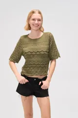 Remera de tejido de punto calado en color natural, con cuello redondo y mangas cortas. Presenta un diseño con texturas de ondas horizontales y terminaciones festoneadas.