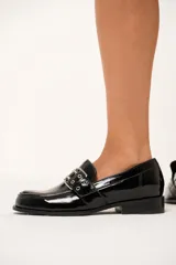 Mocasines negros de charol arrugado con horma redondeada y detalle de presilla con hebilla y ojalillos.