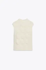 Chaleco de punto en color crudo con cuello subido y manga sisa. Presenta un diseño de tejido con estructura de cables gruesos en el frente y acabados acanalados en el cuello y el bajo.
