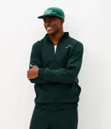 Buzo deportivo Get Over de color verde oscuro, confeccionado en tejido de algodón y poliéster. Presenta cuello alto, cierre frontal completo con cremallera, mangas largas con puños ajustados y bolsillos laterales. Incluye un pequeño lettering bordado en el pecho.