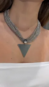 Gargantilla compuesta por múltiples cadenas finas de eslabones plateados que se unen en un dije central con forma de triángulo invertido de superficie lisa y brillante.